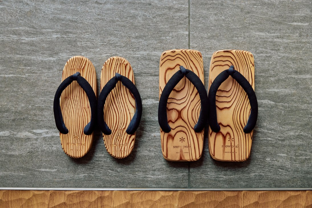 Two pairs of Snow Peak branded wooden sandals with black straps on wooden flooring