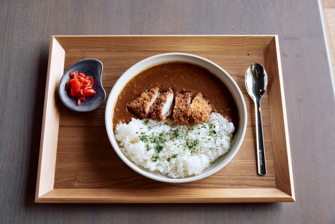 Katsu curry bowl with breaded cutlet, white rice and curry sauce served on wooden tray with pickled vegetables