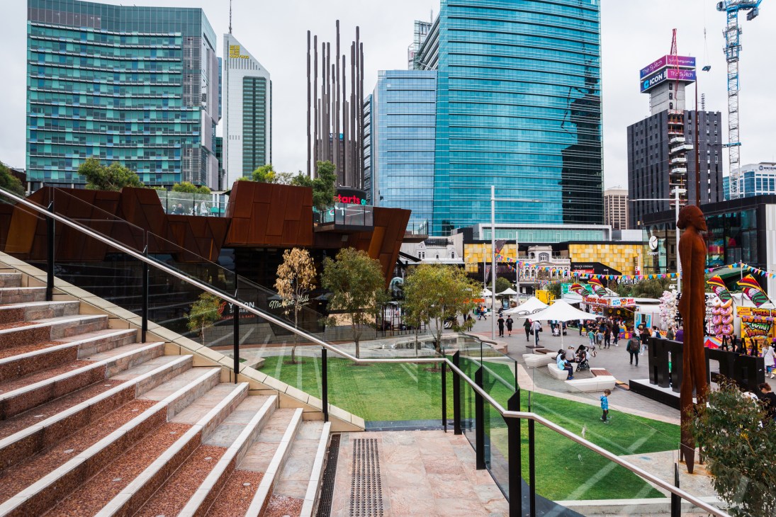 Modern urban square with stairs, green lawns, people walking and gathering in pedestrianized public space