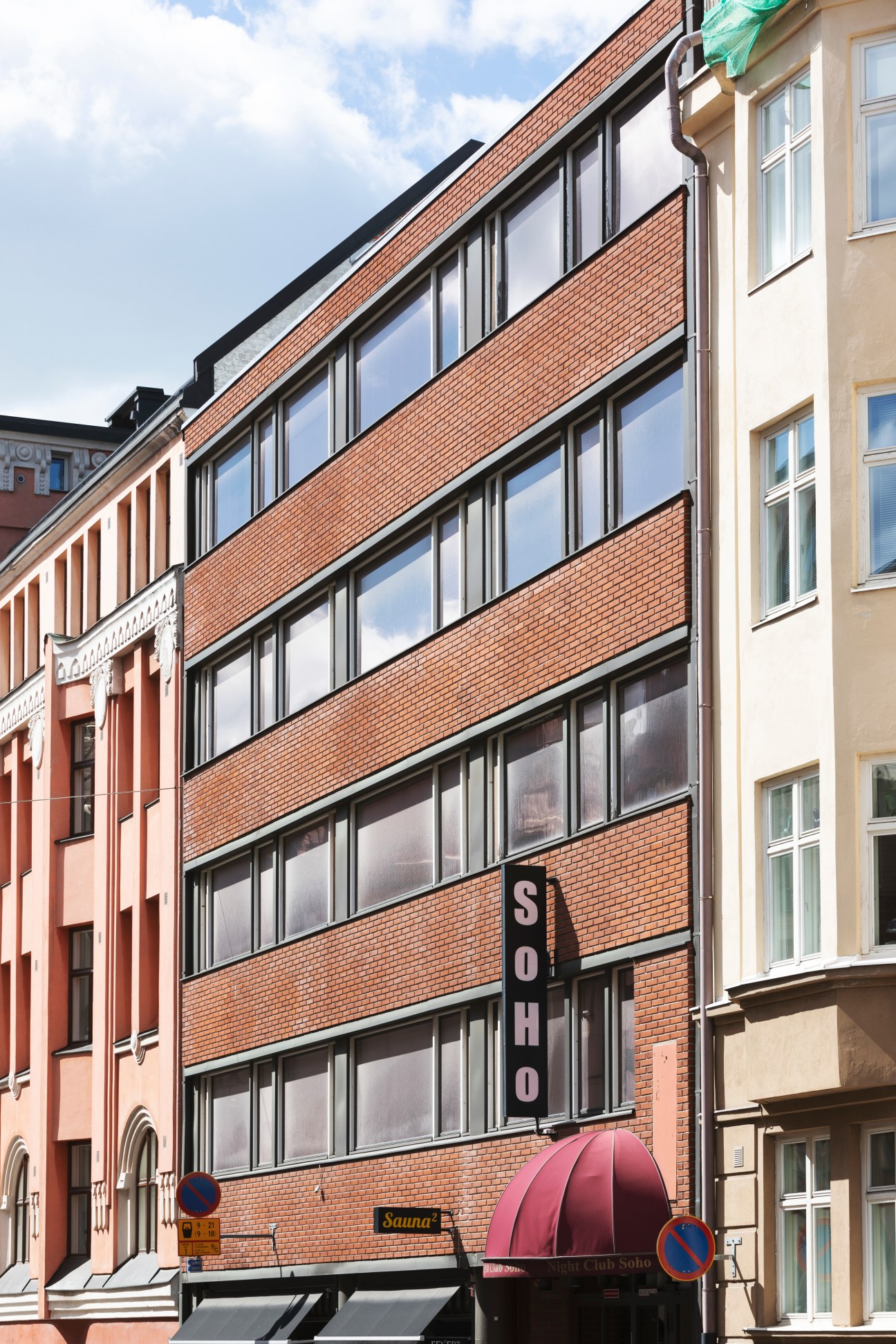 Multi-story brick building with large windows and red awning on street in Helsinki