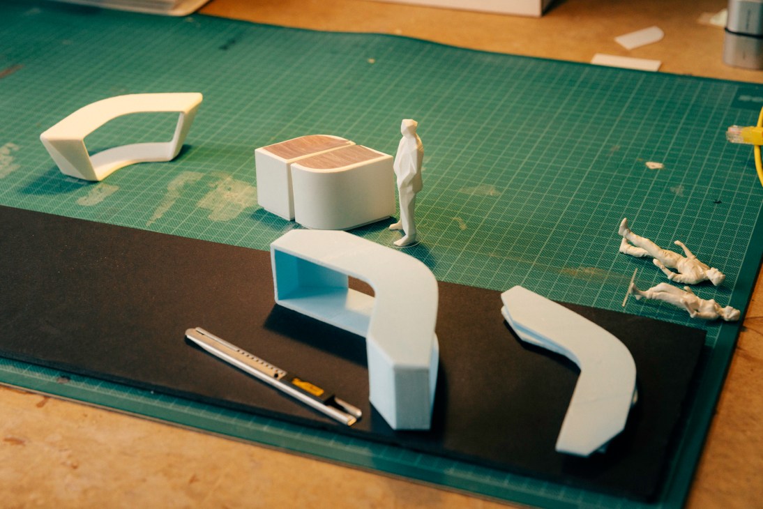 White 3D printed model furniture pieces and figure on green cutting mat in design studio workspace