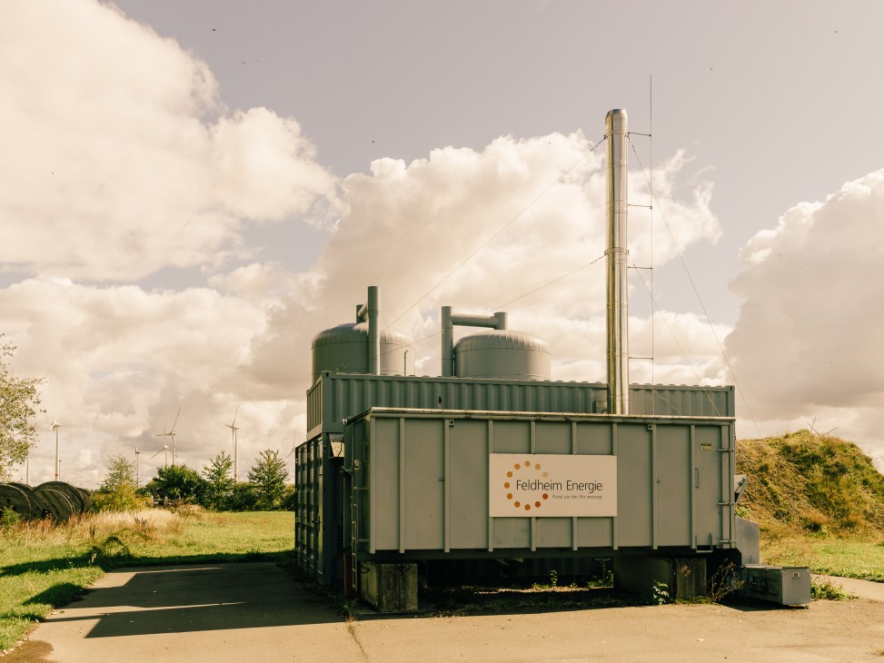 Feldheim Energie biogas plant with green industrial containers and tall metal tower under cloudy sky