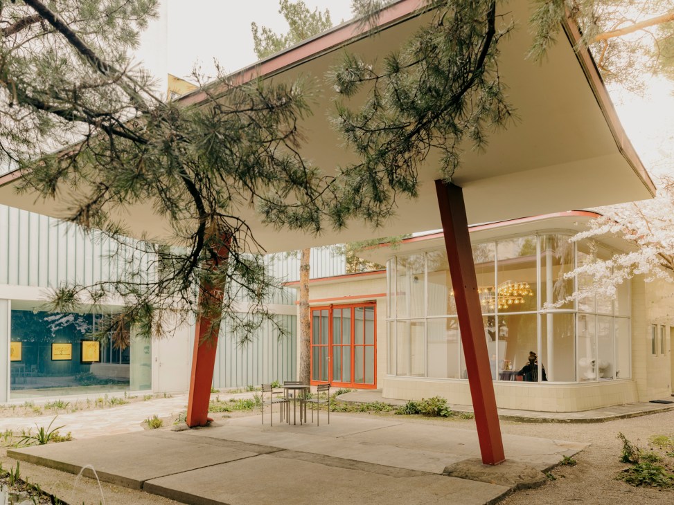Modern architectural renovation of a former 1950s petrol station with cream exterior, red support columns, and large windows.