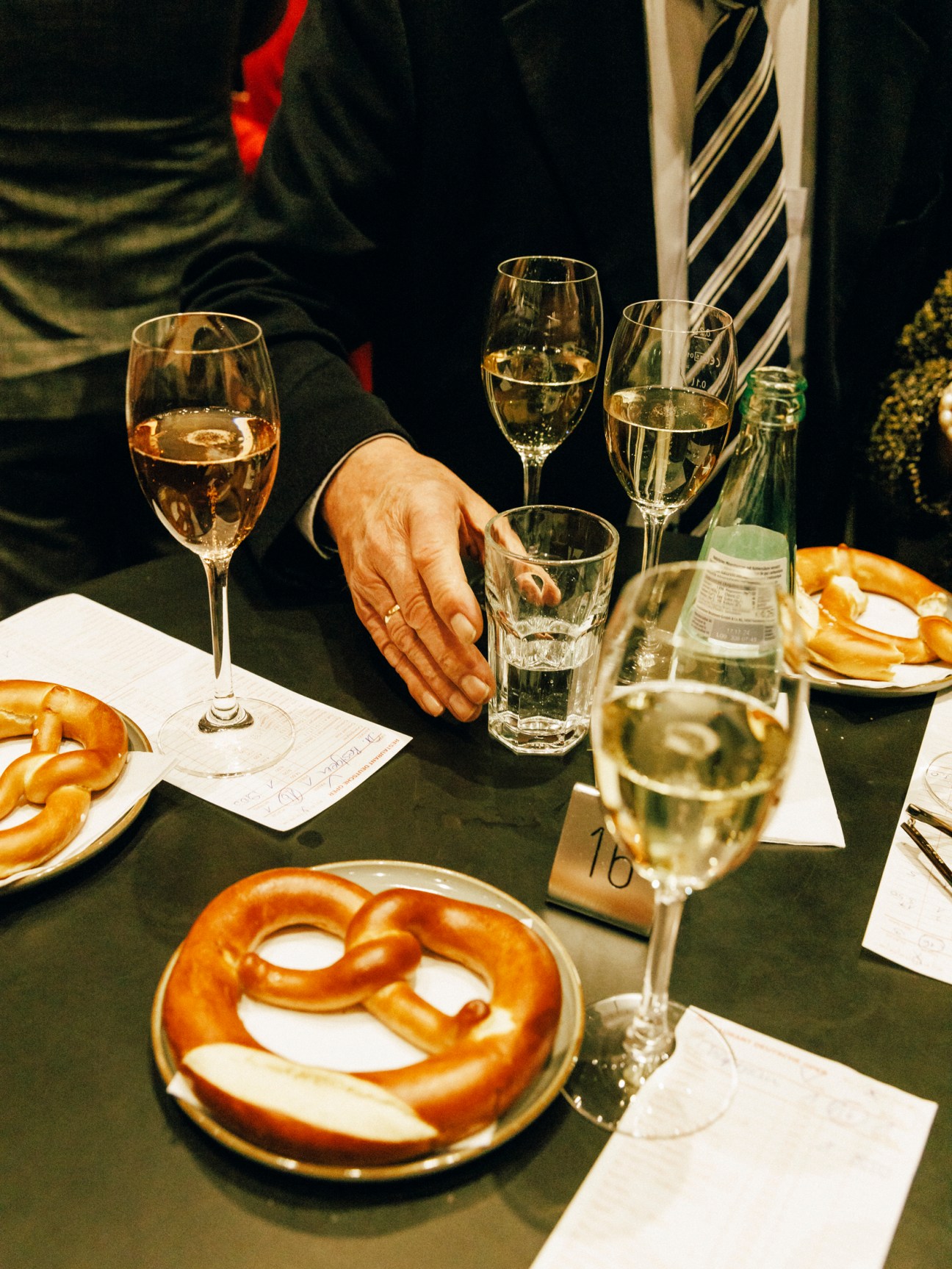 People enjoying champagne and pretzel snacks at a table during an opera interval.