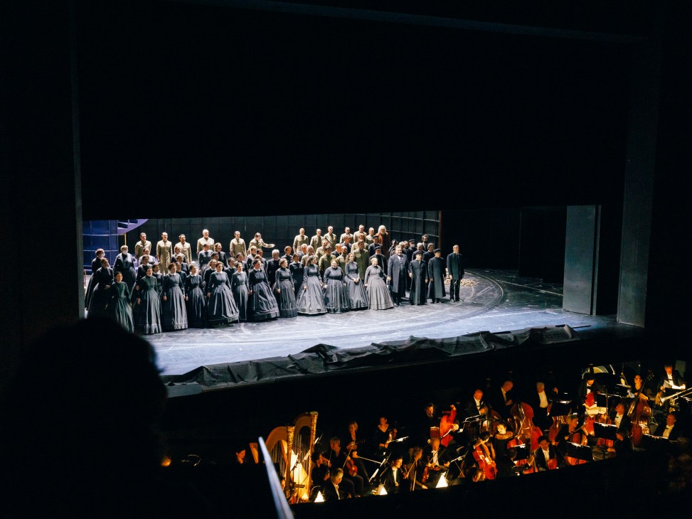 Chorus performers in period costumes on stage during a performance of Verdi's opera Nabucco at Deutsche Oper Berlin, with orchestra visible in pit below.