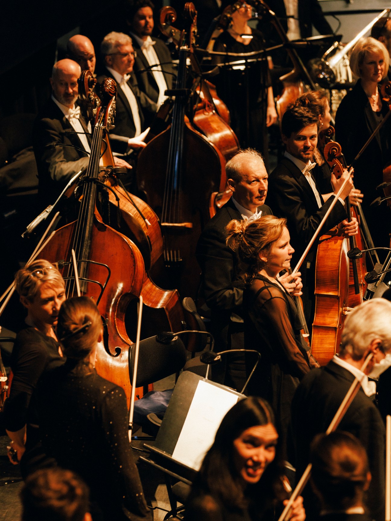 Orchestra string section with cellists and violinists in formal attire performing on stage.