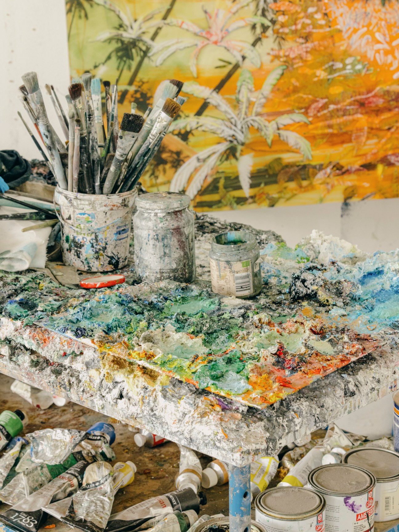 Artist's studio workspace with paint-covered palette and brushes in jars