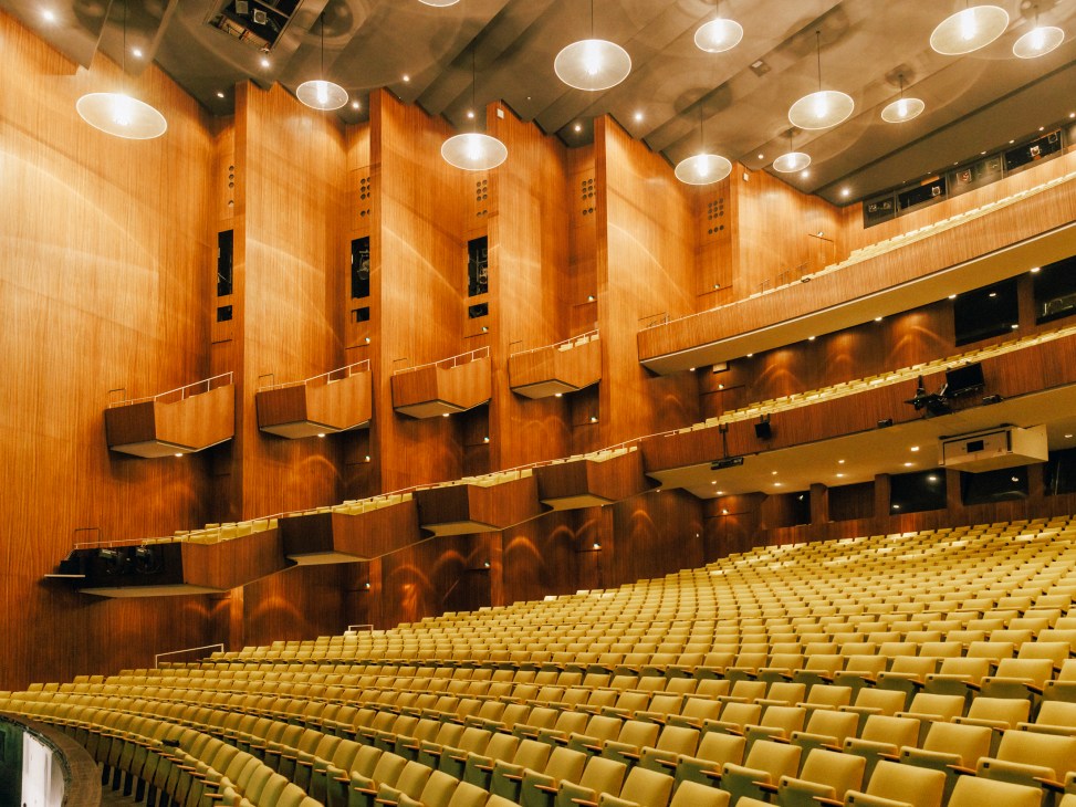Deutsche Oper's modernist auditorium with wooden wall panels, yellow seats, and circular ceiling lights.