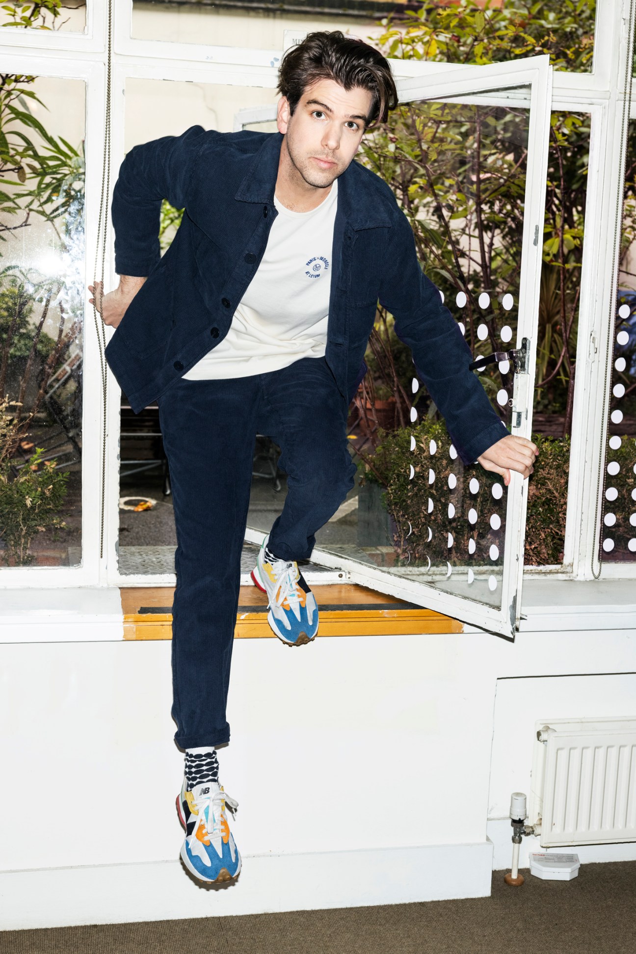 Nic Monisse wearing navy cord overshirt from La Paz, stepping through white doorway with colorful sneakers