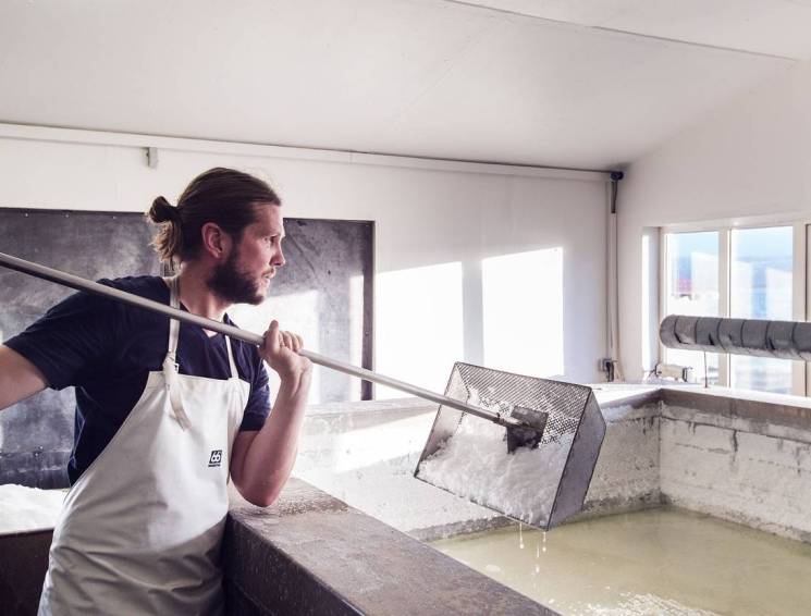 Man in white apron stirring salt production using geothermal energy in Icelandic facility.