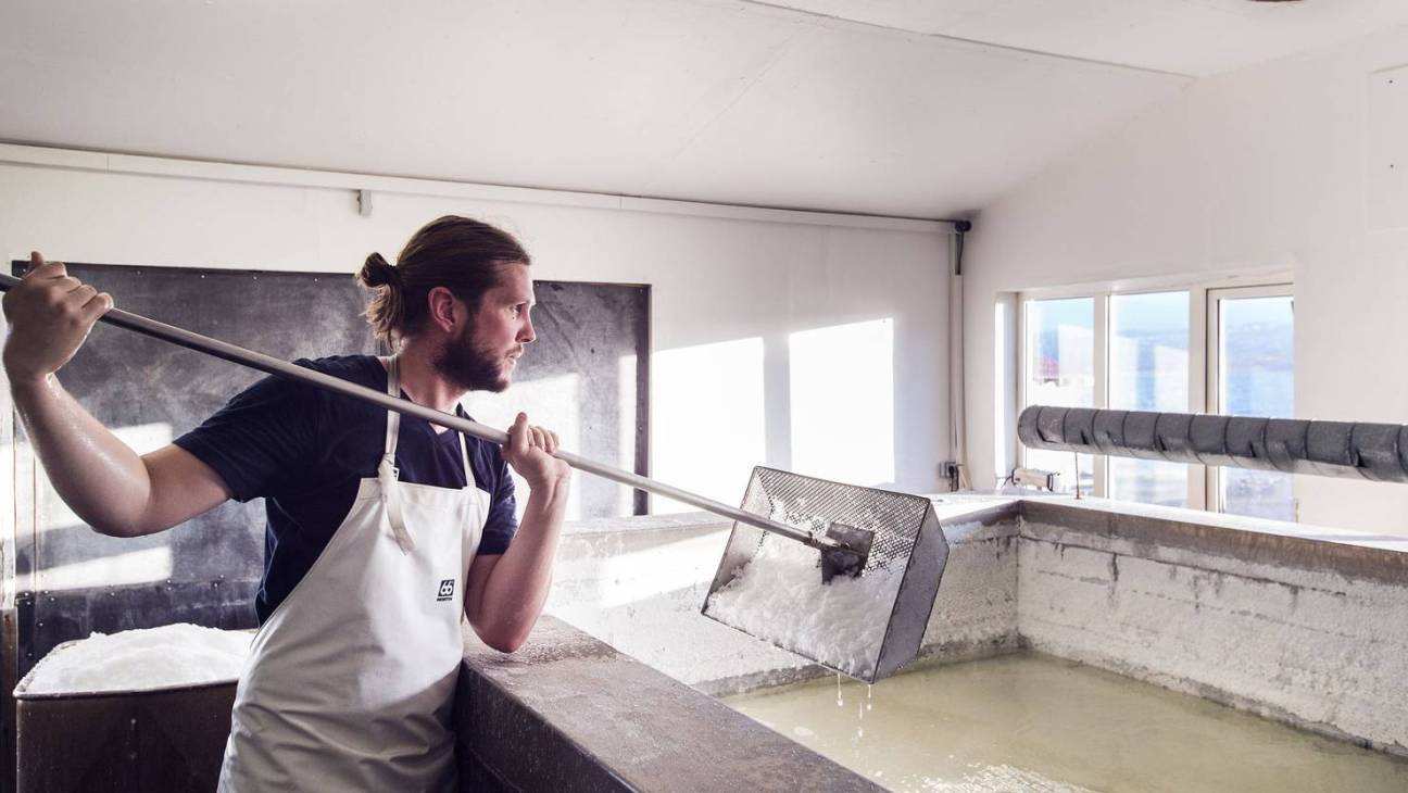 Man in white apron stirring salt production using geothermal energy in Icelandic facility.