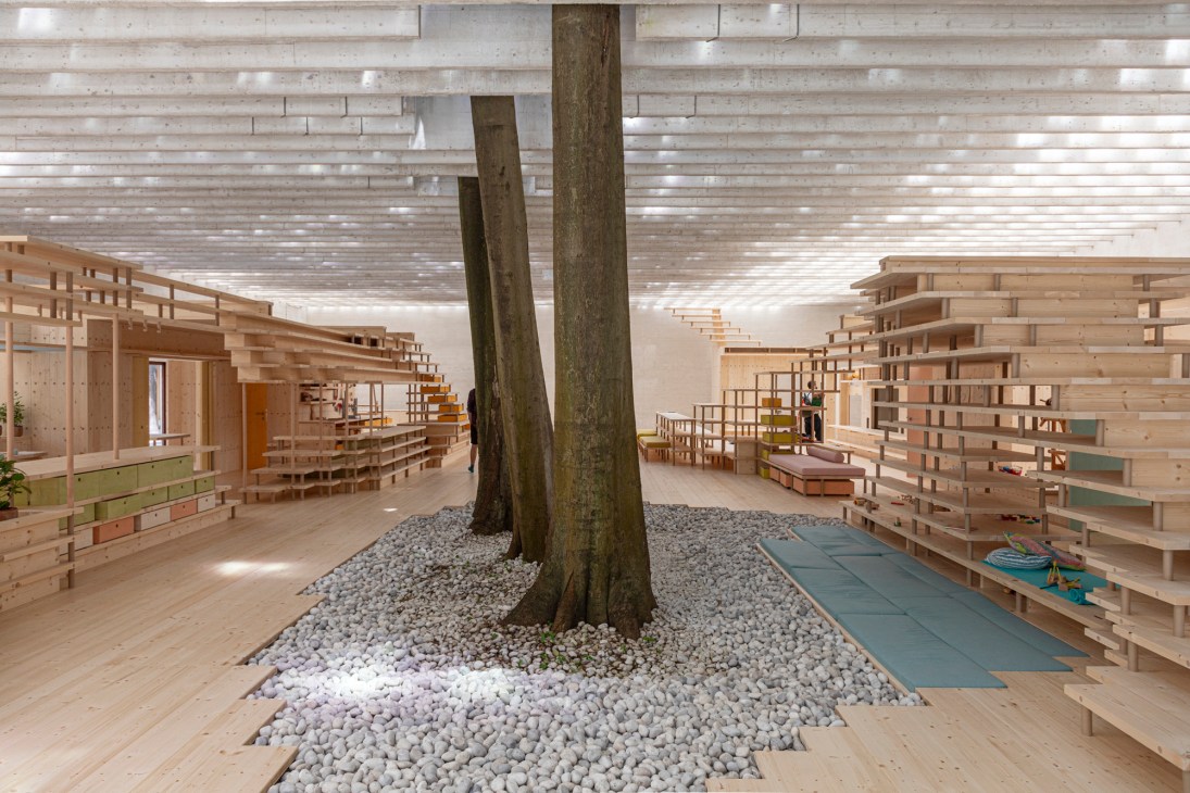 Interior of Nordic pavilion at Venice Architecture Biennale with wooden shelving, natural tree trunks, and light-filled ceiling.