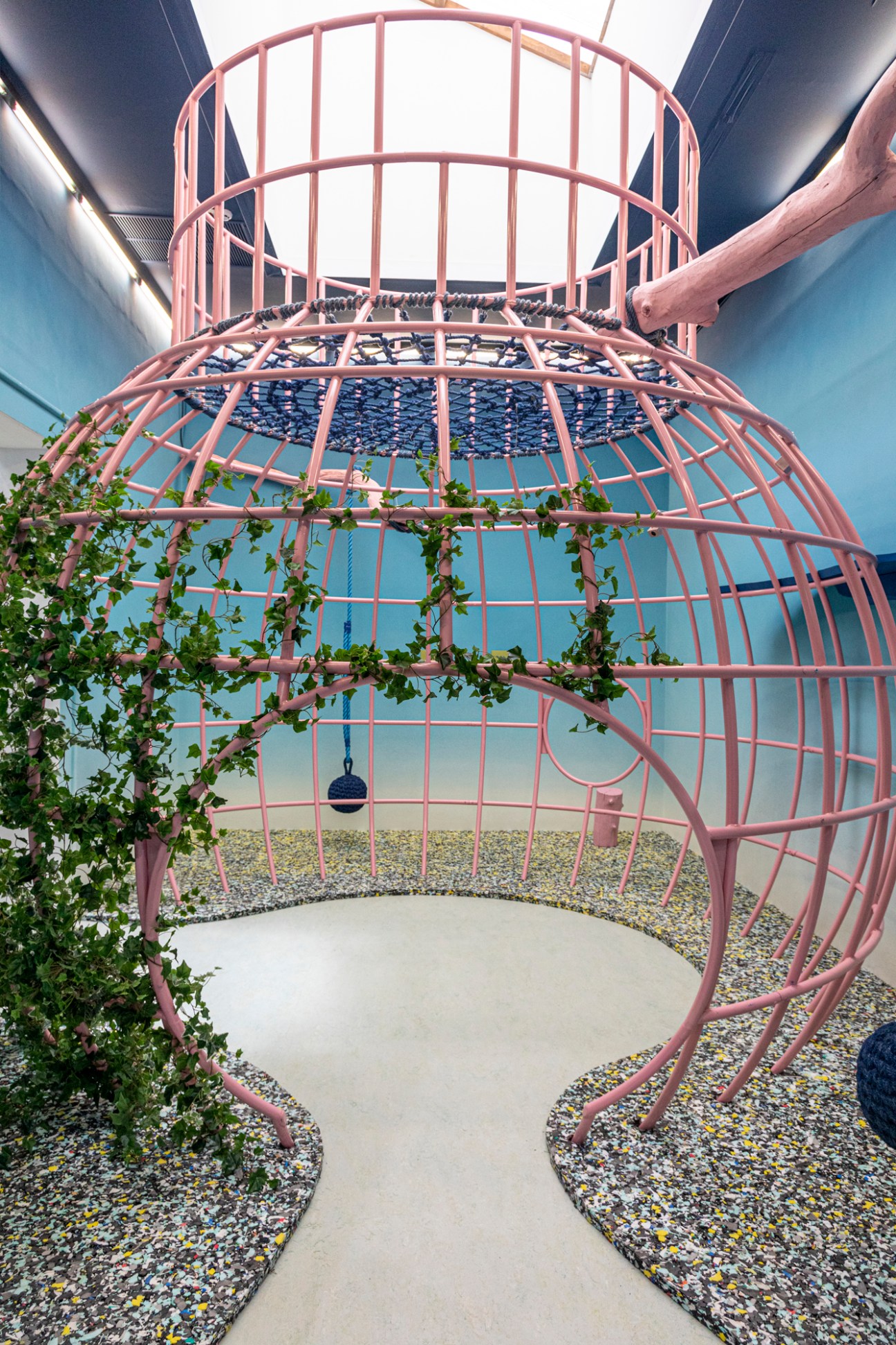 Interior of UK pavilion with pink metal framework, climbing vines, and gravel floor beneath glass ceiling.