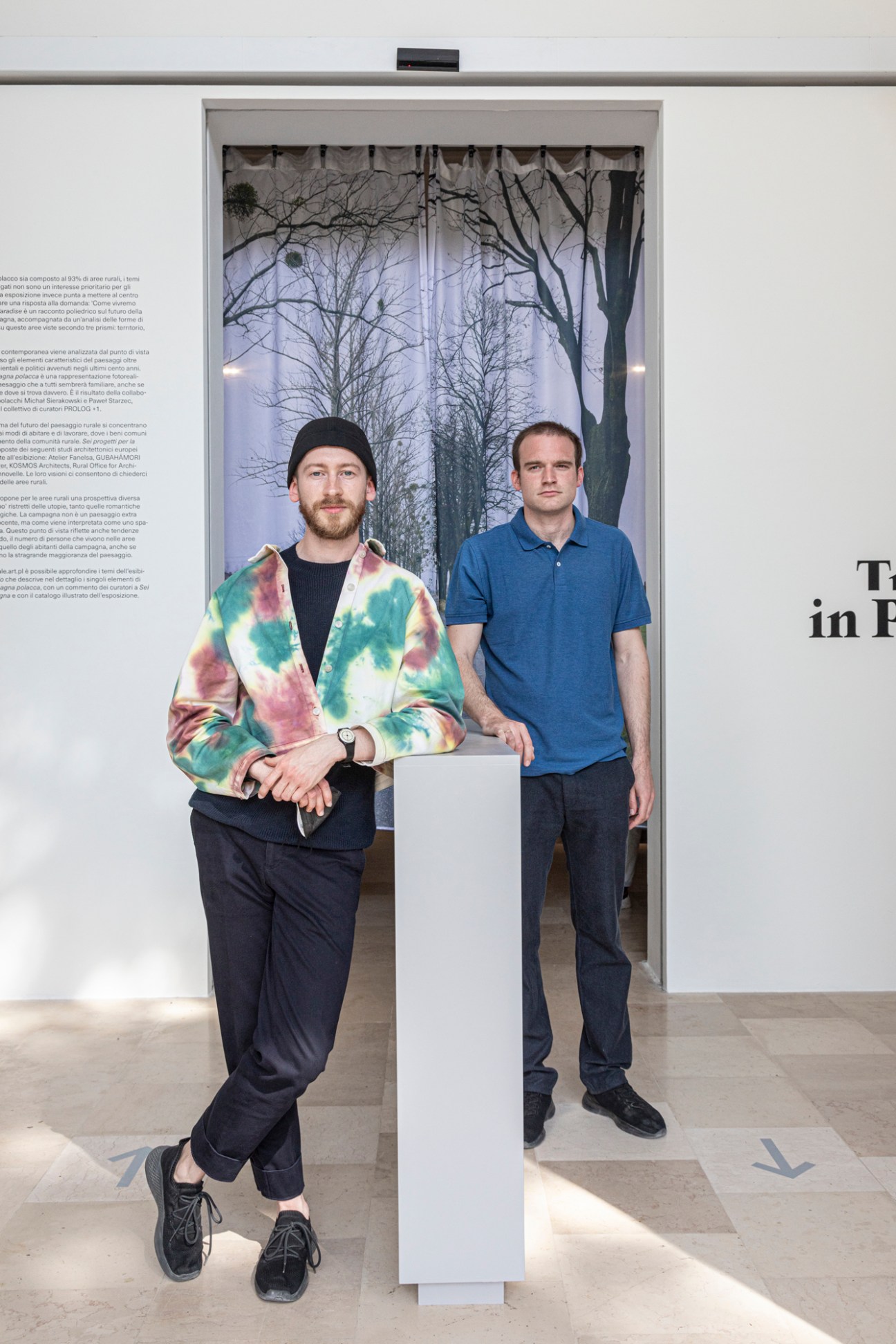 Poland pavilion curators Rafal Sliwa and Bartosz Kowal stand in front of a backlit forest installation.