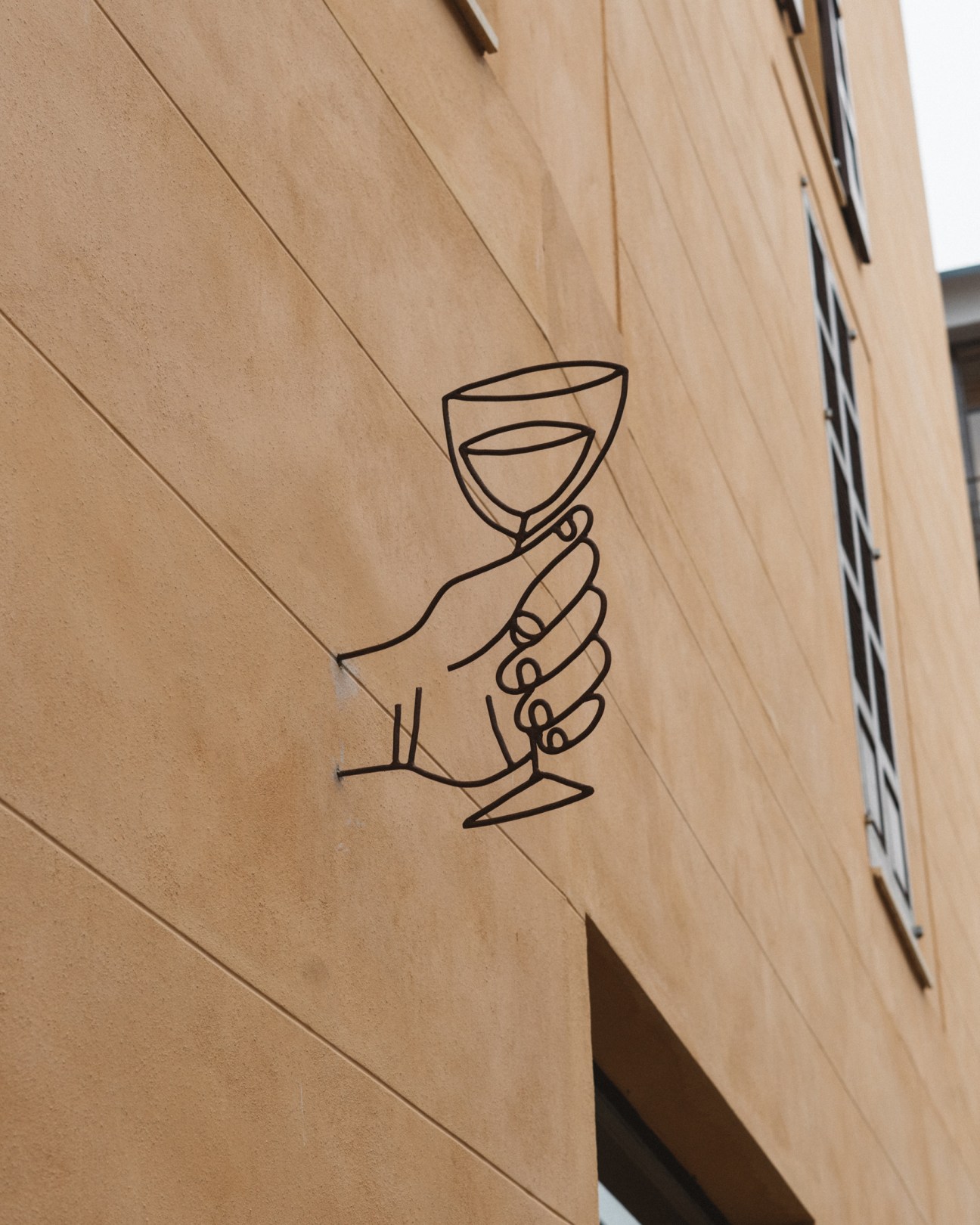 Line drawing of a hand holding a wine glass on wooden surface at Cav wine shop
