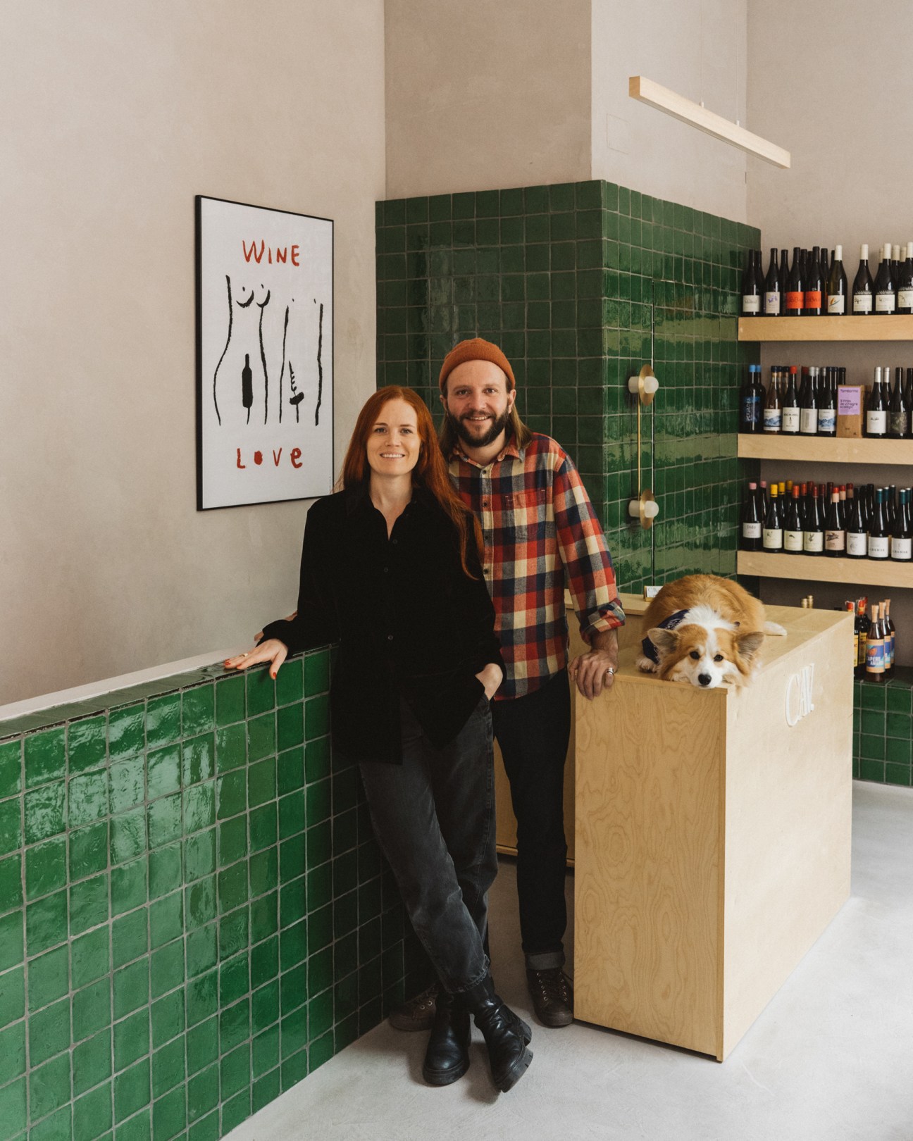 Lauren and Charlie Prymaka standing in their wine shop Cav with their corgi Bao on the counter