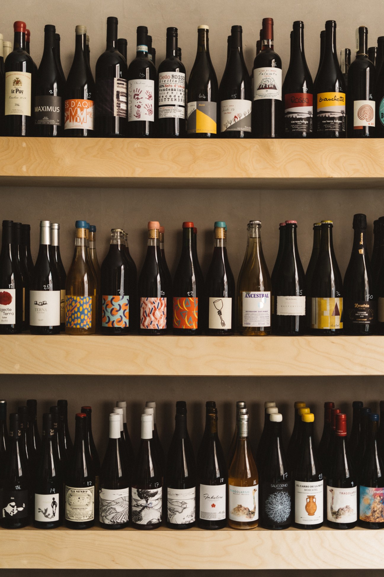 Three shelves displaying rows of wine bottles with colorful labels and various closure types