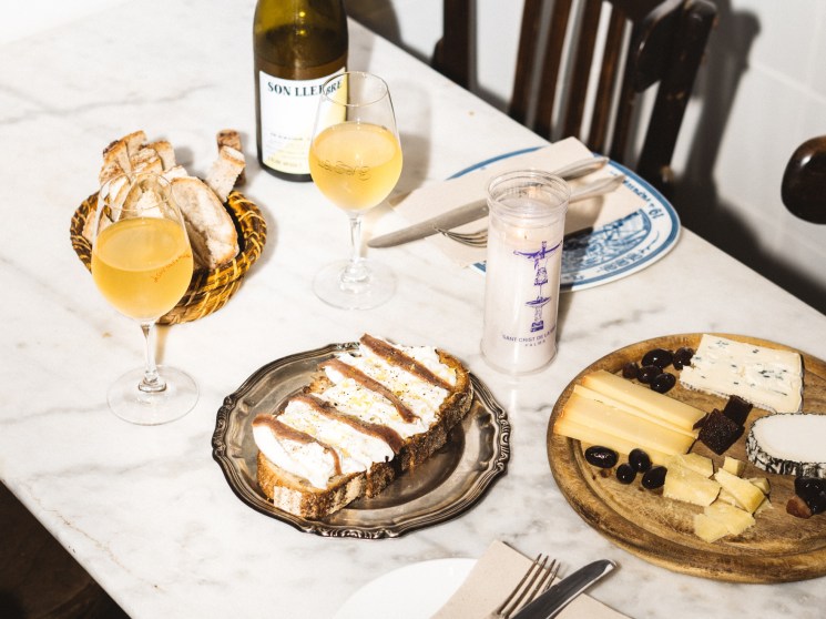 Table setting with white wine, cheese board, bread basket, and mozzarella and anchovies on fresh bread