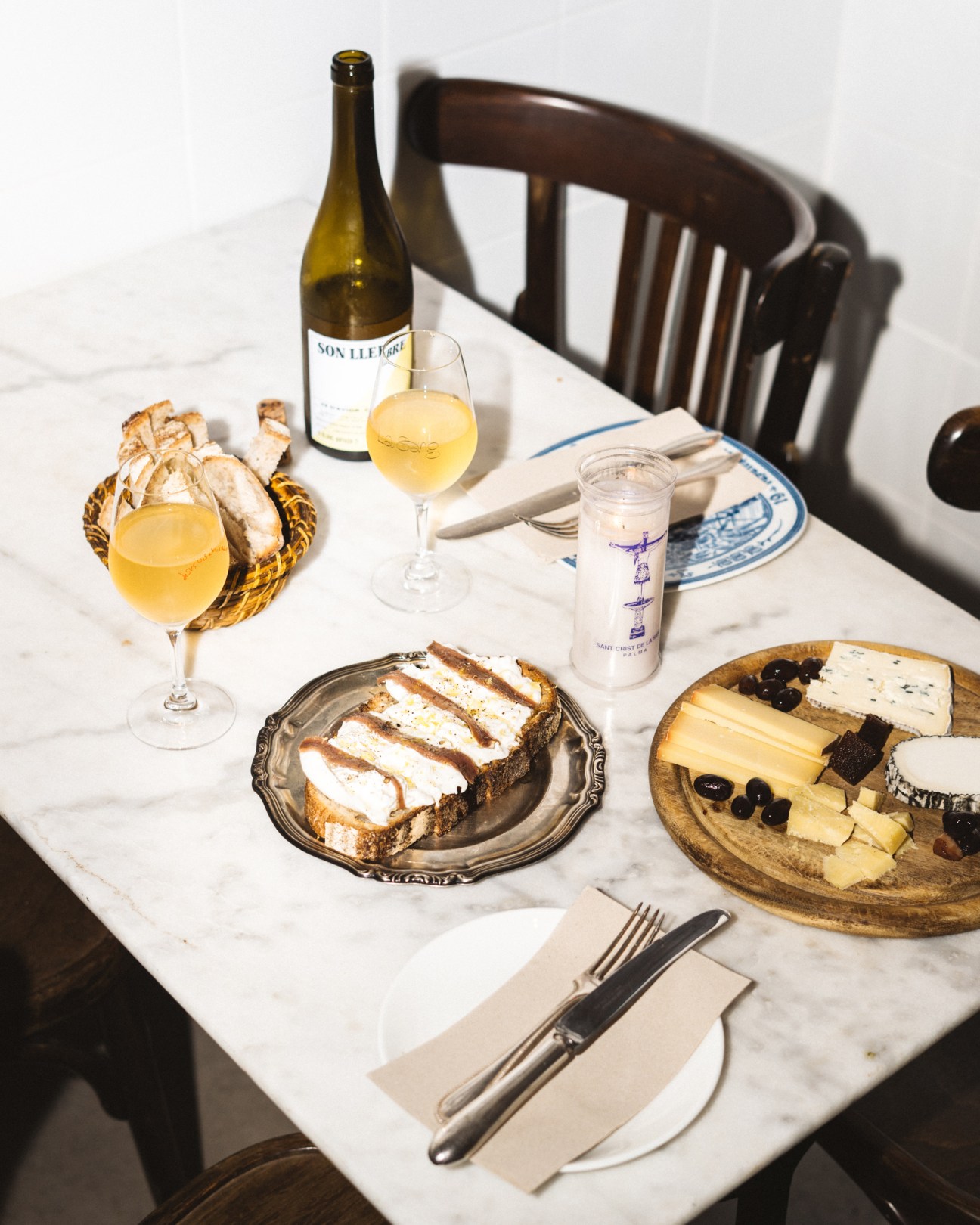 Table setting with white wine, cheese board, bread basket, and mozzarella and anchovies on fresh bread