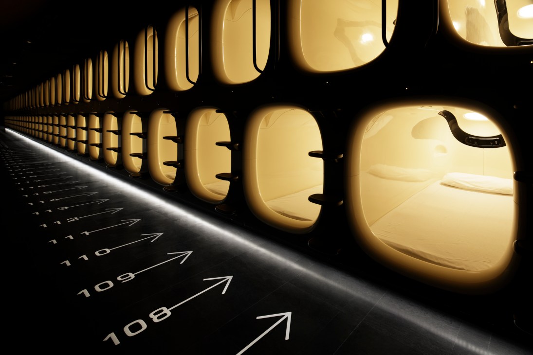 Row of illuminated capsule hotel sleeping pods with white bedding and rounded openings