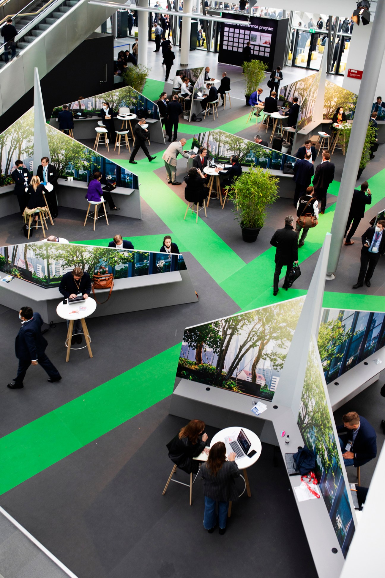 Aerial view of a trade fair exhibition space with green pathways, meeting areas, and attendees networking