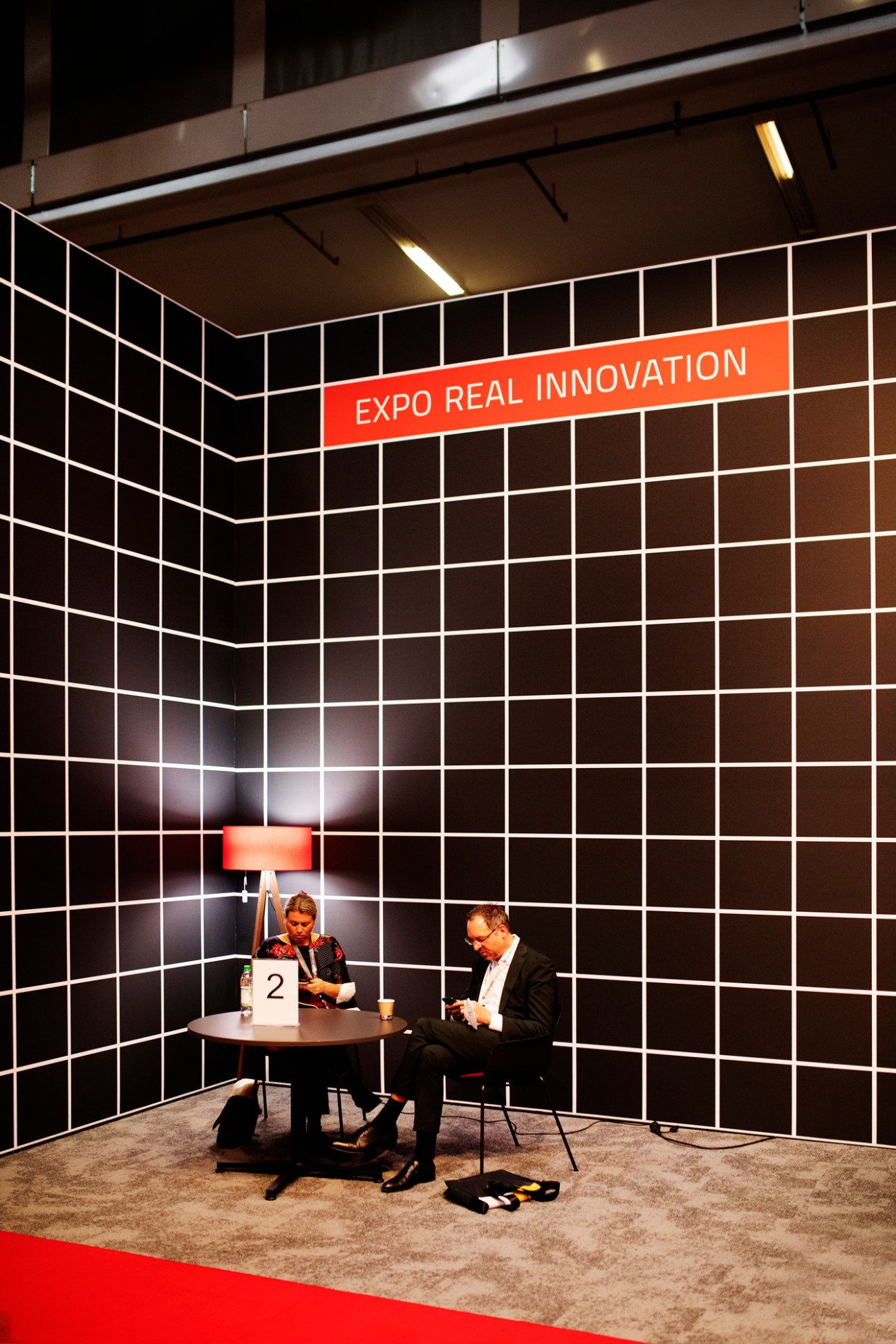 Two business people sitting at a table in a corner booth, both looking at their mobile phones