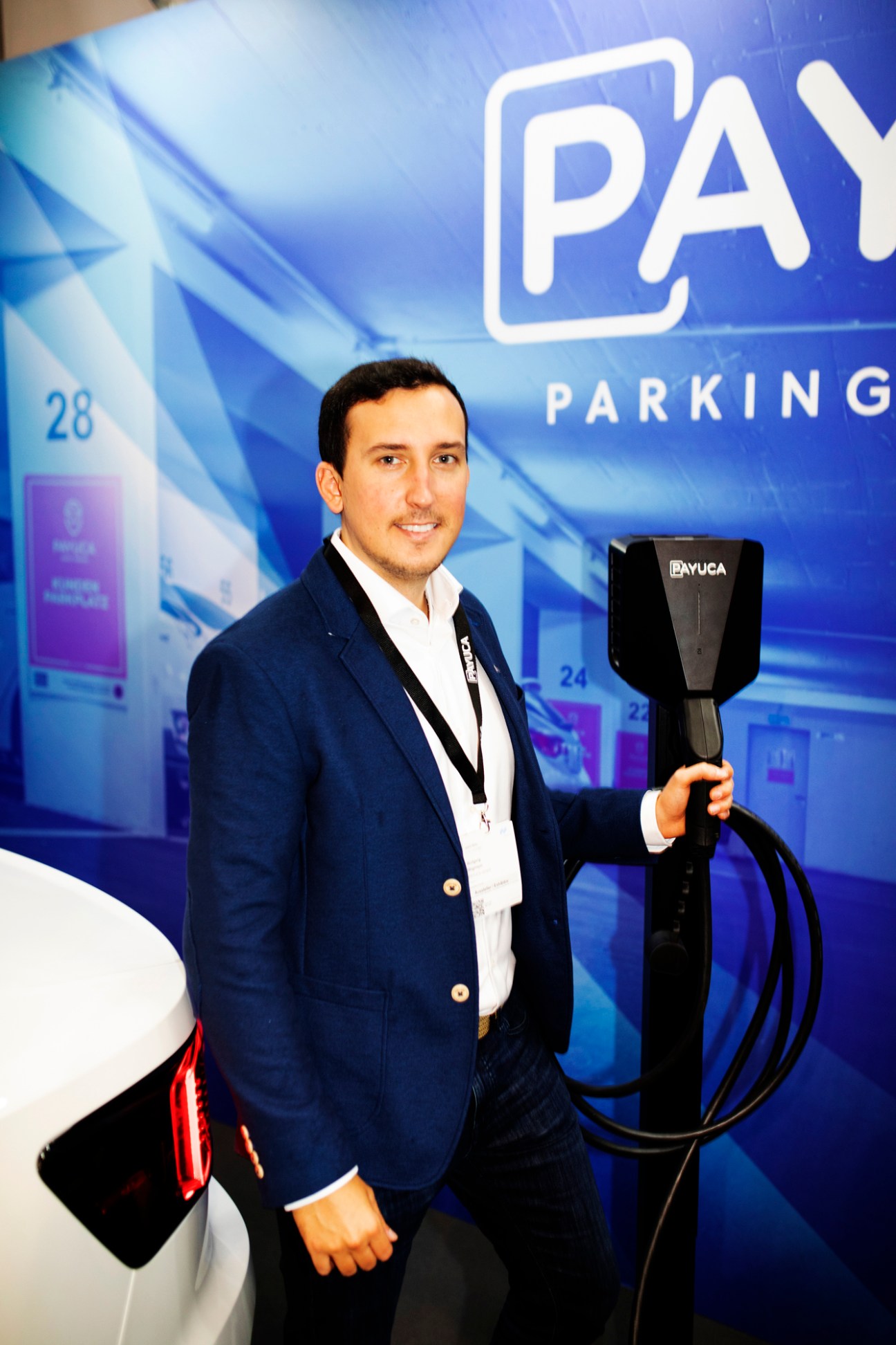 Wolfgang Wegmayer of Payuca standing next to an electric vehicle charging station at a trade fair booth