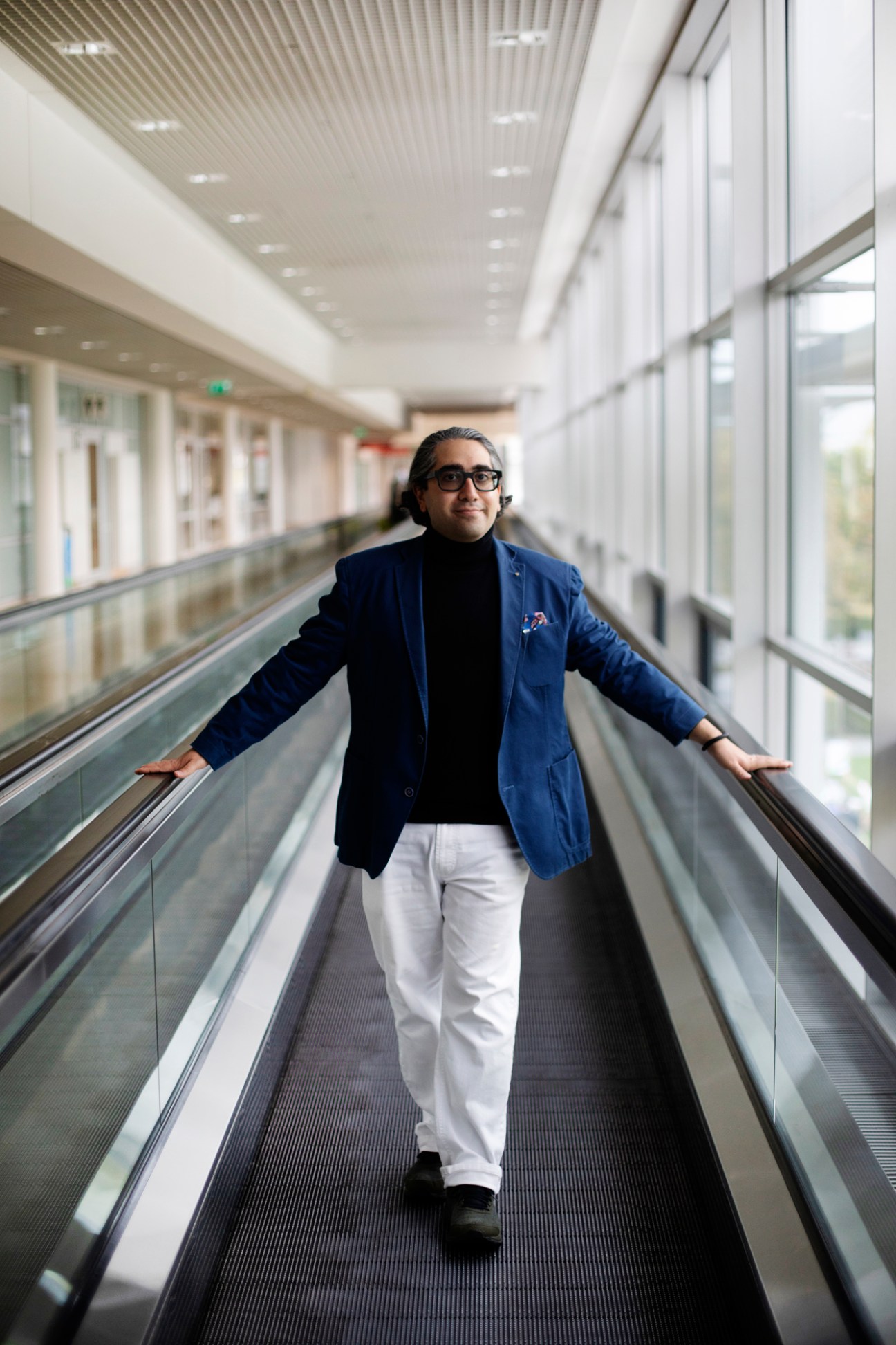 Manouchehr Shamsrizi of Berlin Humboldt University standing on a moving walkway in a modern building corridor
