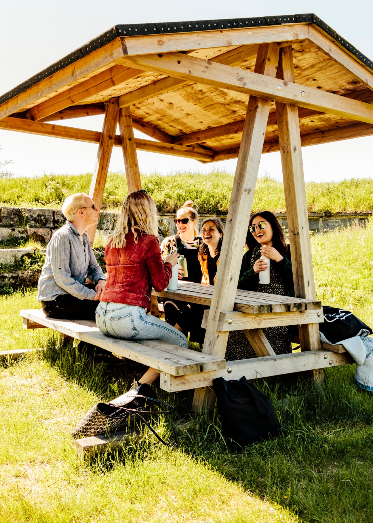 Visitors gather under a wooden shelter on grass at Vallisaari island during the Helsinki Biennial.
