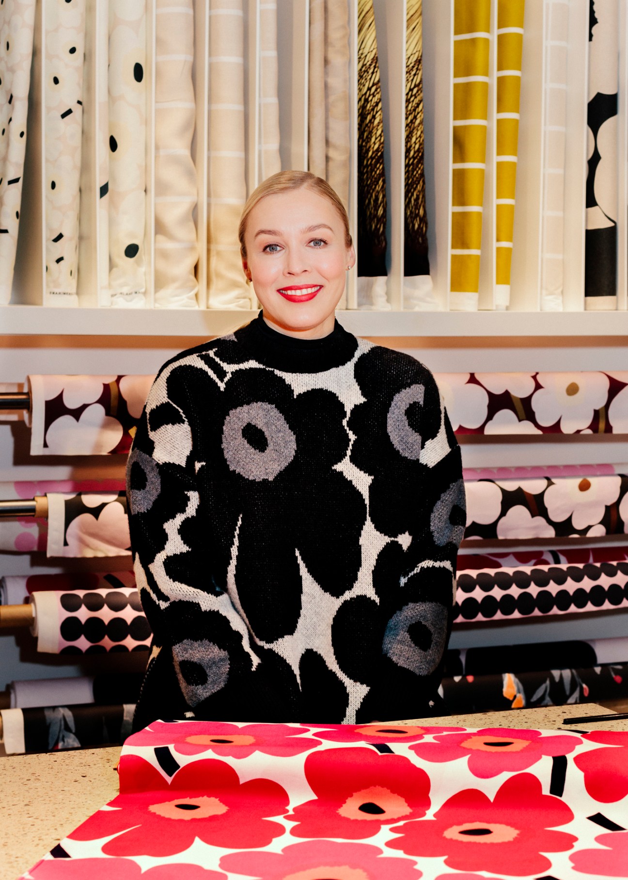 CEO Tiina Alahuhta-Kasko wearing a black and white patterned sweater, sitting in front of colorful fabric displays