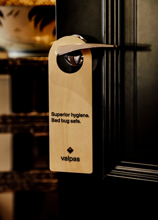 Valpas bed leg door hanger with text 'Superior hygiene. Bed bug safe.' hanging on hotel door.