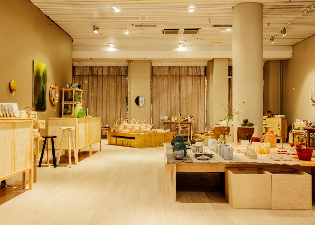 Interior of Lokal Aleksi design shop with wooden furniture, ceramics and home goods displayed throughout a minimalist light wood space.