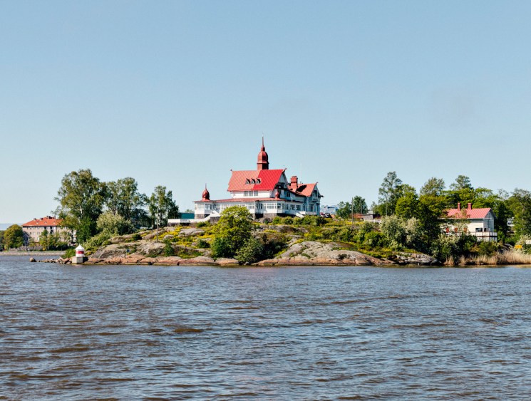 Red-roofed manor house on a small rocky island in calm water.