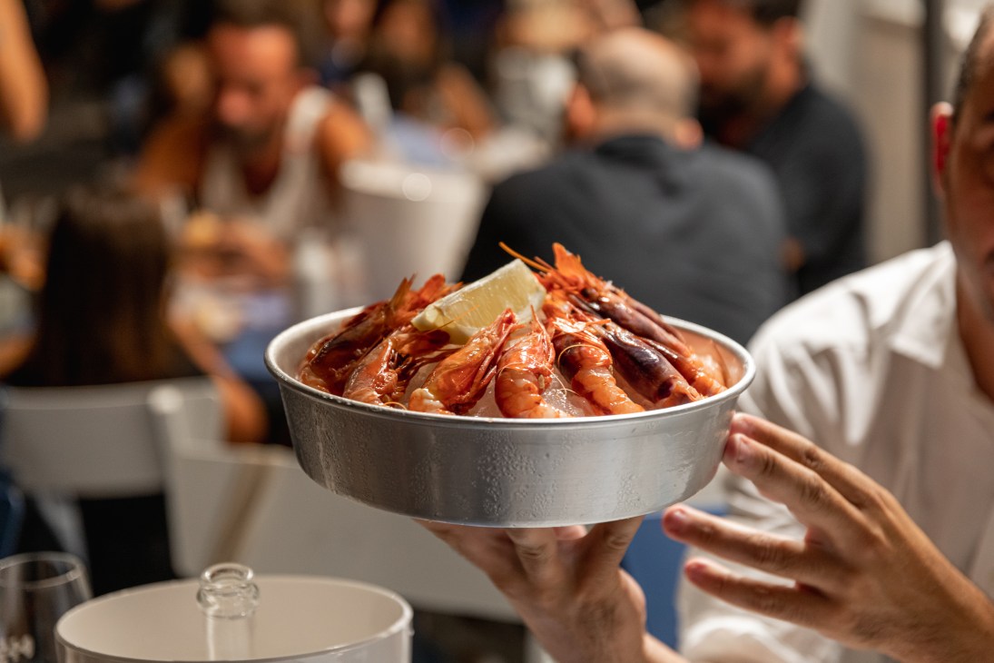 A server holds a metal bowl of cooked prawns garnished with lemon at Pescaria restaurant in Rome.