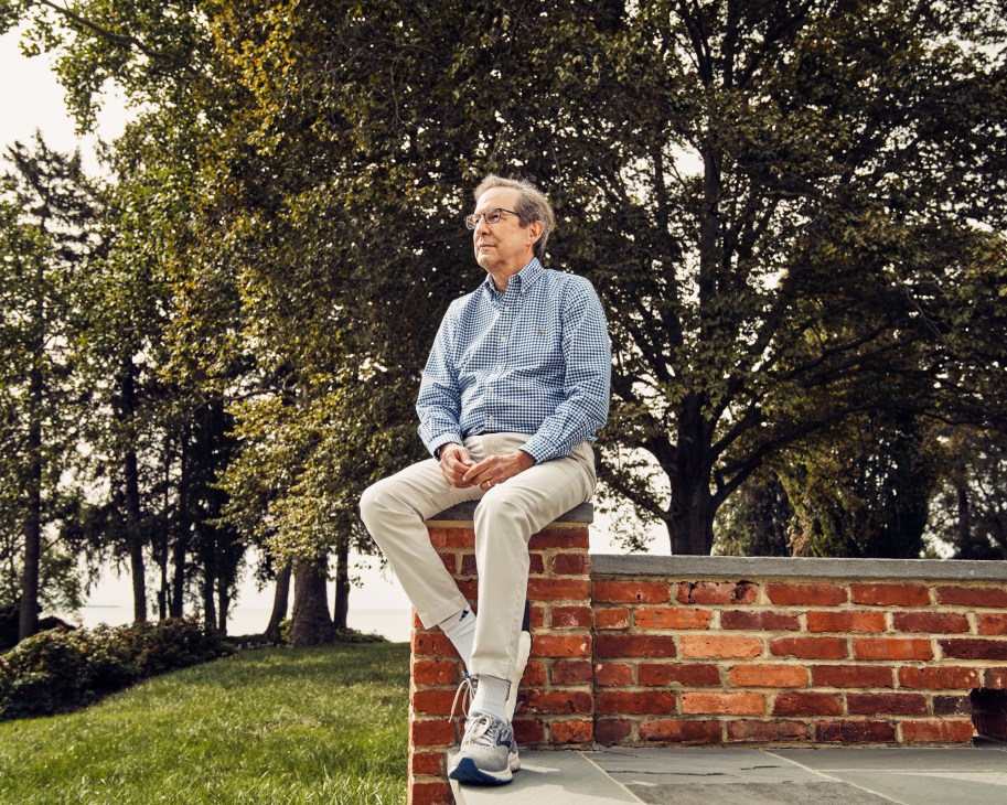 Chris Wallace sitting on brick wall outdoors wearing checkered shirt and khakis