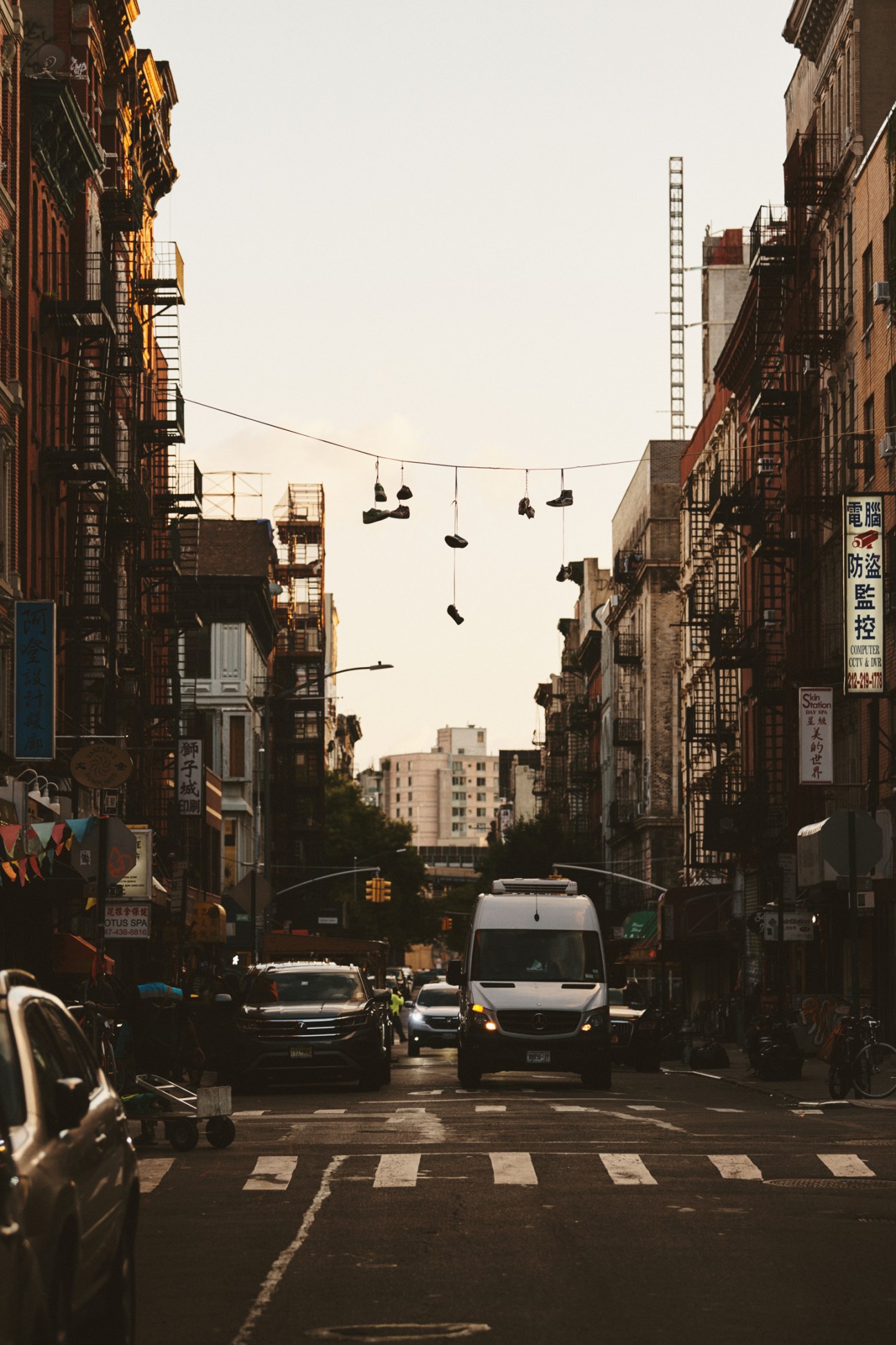 New York City street scene with brick buildings, hanging shoes, parked cars and pedestrian crossing.