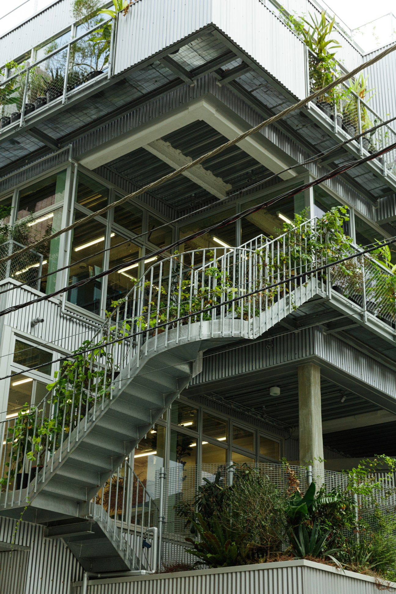 Multi-storey modern building with green plants on multiple balconies and exterior metal railings.