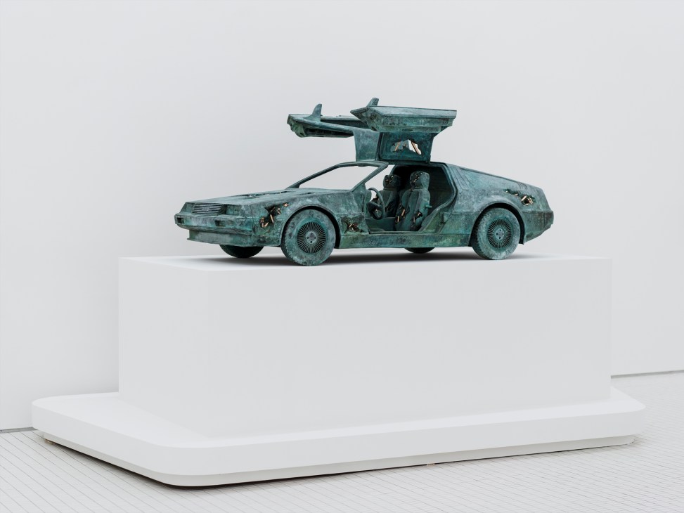 Oxidized bronze sculpture of DeLorean car with gull-wing doors open displayed on white pedestal
