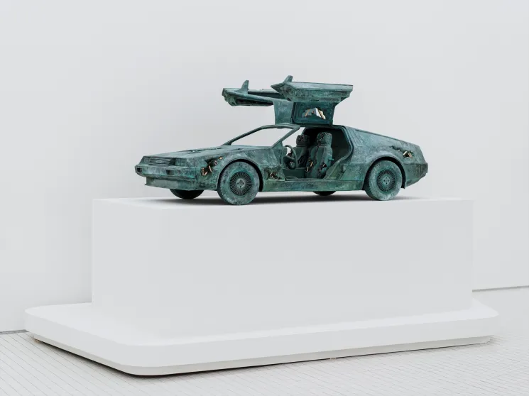 Oxidized bronze sculpture of DeLorean car with gull-wing doors open displayed on white pedestal