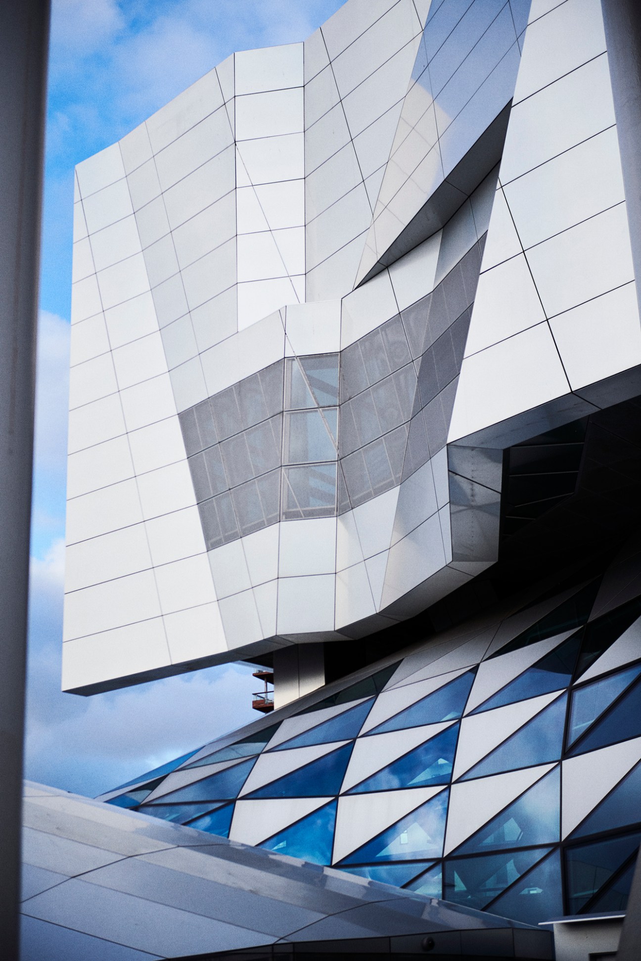 Modern white concert hall with geometric glass and metal facade against blue sky, Musikkens Hus in Aalborg.
