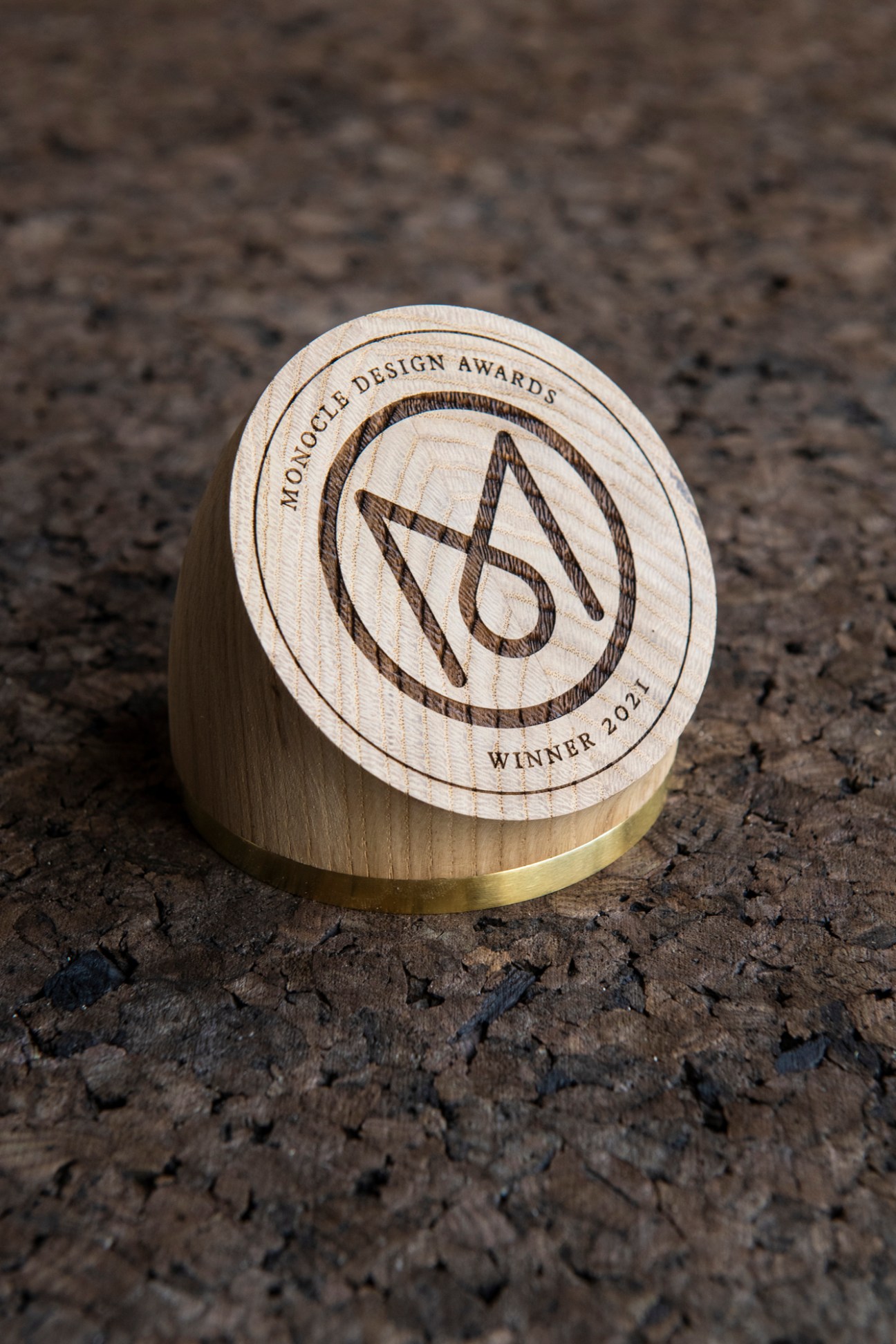 Wooden and brass Monocle Design Awards trophy with engraved circular logo and text.