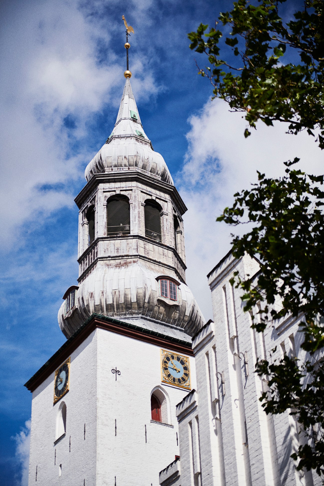 White-walled Budolfi Church with ornate spire and clock face in Aalborg, Denmark.