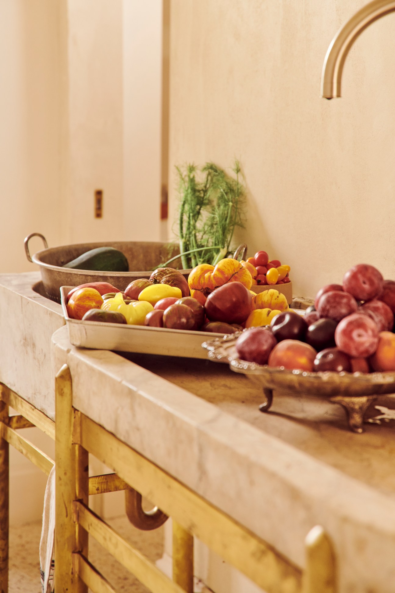 Kitchen counter with fresh produce in wooden trays and a brass faucet above the sink.