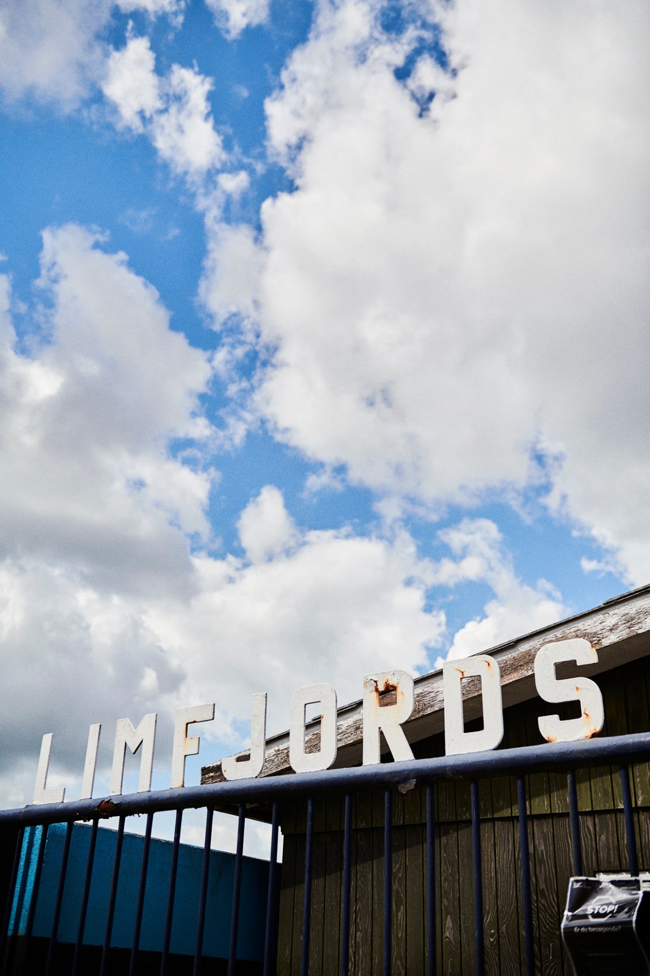 White "Limefjords" sign on weathered wooden building with blue railings under blue sky with clouds.