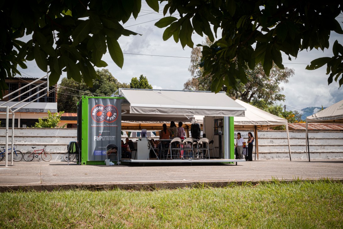 Mobile journalism classroom shipping container with sides folded down and journalists conducting training session