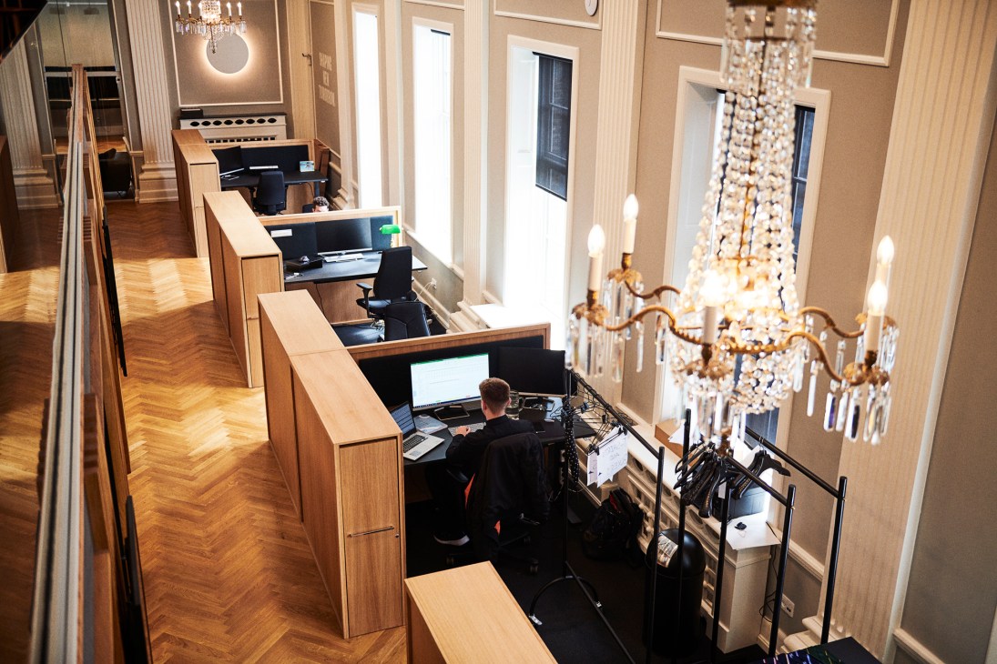 Interior of Shaping New Tomorrow headquarters with wooden workstations, chandeliers, and tall windows in downtown Aalborg.