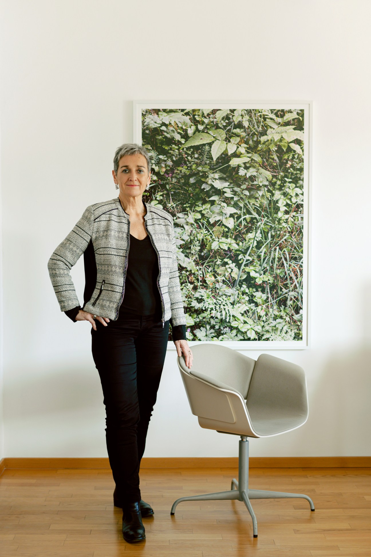 Ulrike Lunacek standing beside a white chair in an office with a large botanical artwork on the wall behind her