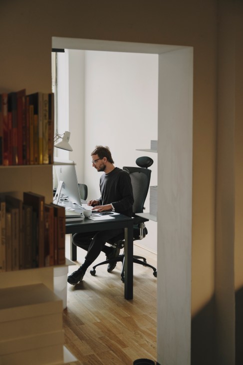 Designer Ingmar Spiller working at a computer in a minimalist office space with bookshelves.