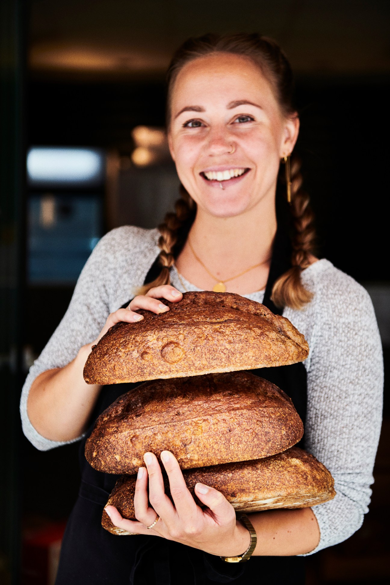 Woman holding three loaves of fresh brown bread from Surdejsbageren bakery in Aalborg, Denmark.