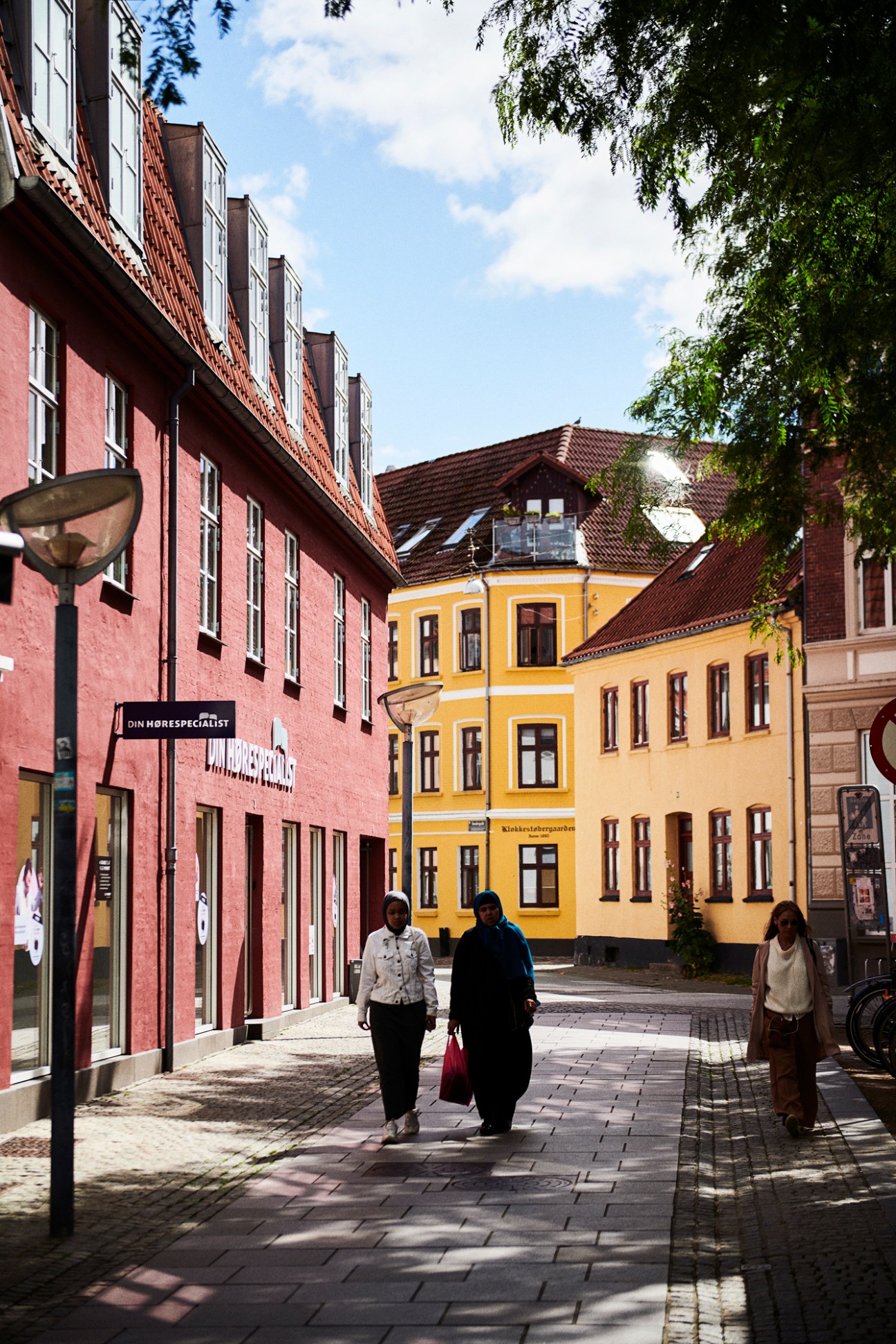 Pedestrians walking down a cobblestone street lined with colorful historic buildings in Aalborg, Denmark.